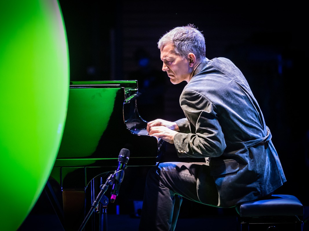 Brad Mehldau 在绿色圆形灯饰前演奏三角钢琴