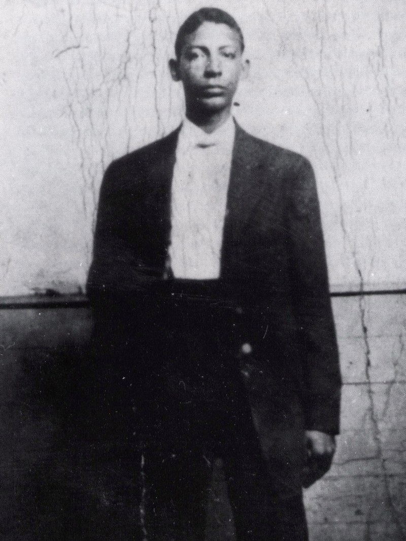 少年时期的 Jelly Roll Morton 全身像，穿深色西装与浅色衬衫，靠墙站立