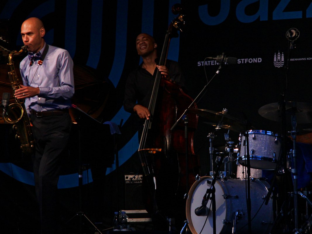 Joshua Redman 在 2014 年哥本哈根爵士音乐节舞台上吹奏次中音萨克斯，左侧近景，身后是贝斯手与鼓手