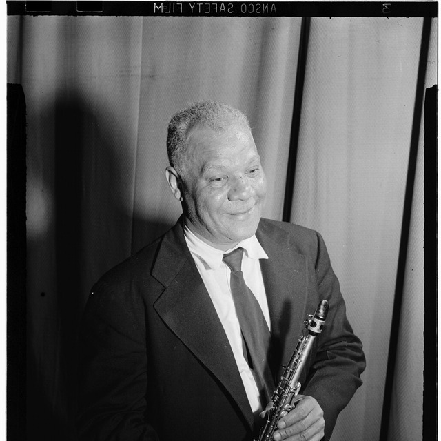 西德尼·贝谢（Sidney Bechet）1946 年 7 月在纽约的肖像，穿深色西装打领带，右手扶着单簧管，背景为浅色幕布